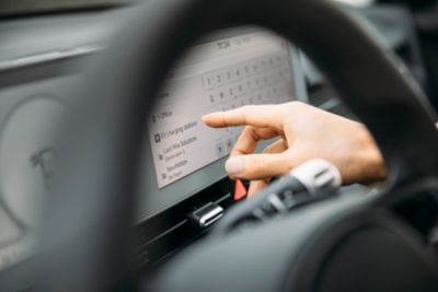 Kierowca samochodu IONIQ 5 wybiera stację ładowania na ekranie centralnym wewnątrz pojazdu.