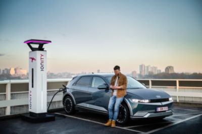 The Hyundai IONIQ 5 plugged into charging station on a wide open parking lot.