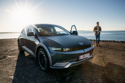 Elektromobil Hyundai IONIQ 5 a jeho řidič stojící na pláži.