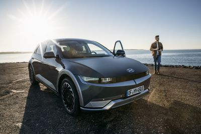 Hyundai IONIQ 5 aparcado en la playa con un hombre de pie junto a él.