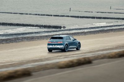 The Hyundai IONIQ 5 electric vehicle driving on a beach next to the ocean.