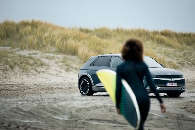 A surfer approaching her Hyundai IONIQ 5 electric vehicle parked on the beach.