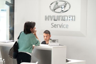 Donna di schiena con glof verde acqua e pantaloni neri aspetta allo sportello Hyundai Service