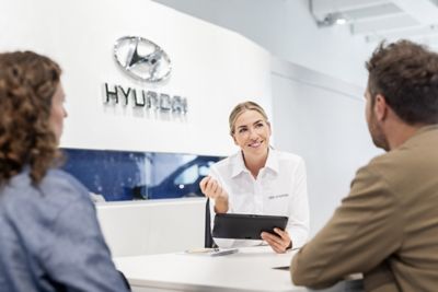Ein Mitarbeiter eines Hyundai Autohauses berät eine Frau und einen Mann an seinem Schreibtisch.