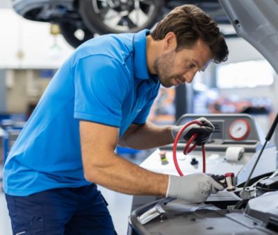 Person sitting in a car holding smartphone. The car dashboard with a large screen and controls is visible in the background.