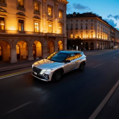 Hyundai TUCSON parcheggiata su una strada cittadina, con una donna in piedi ritratta di fronte al veicolo 