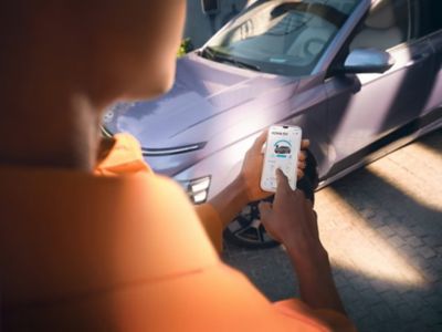 A person using a smartphone and Hyundai Bluelink app in front of a Hyundai KONA.