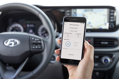 Hand holding a smartphone inside the Hyundai i10 using the BlueLink app.