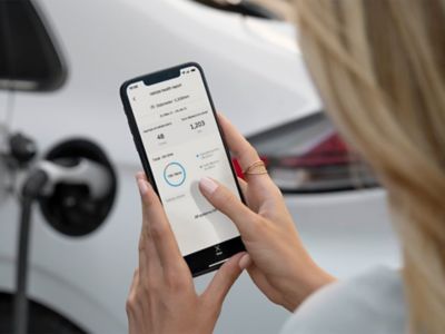 Eine Frau regelt mit Hilfe der Bluelink-App auf ihrem Smartphone das Aufladen ihres Hyundai.