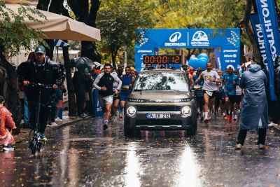 Yüksek ofis binaları arasındaki boş bir caddede bir kolunu kaldırmış hızla koşan iki koşucu. 