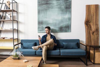 A man sitting on a sofa checking his myHyundai app on his phone.