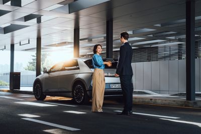 Imagen de dos personas cerrando un trato frente a un IONIQ 5 con una puesta de sol de fondo.