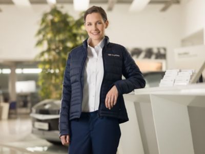 Pracovnice servisu Hyundai v uniformě, opírající se o pult v zákaznické zóně.