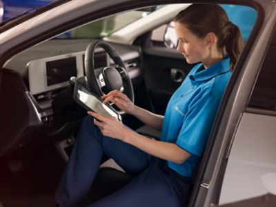 Zamestnanec Hyundai sediaci v automobile používajúci diagnostické zariadenie na kontrolu elektrického pohonu.