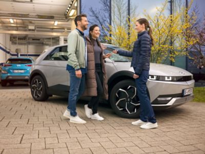 A Hyundai staff member in blue uniform giving a car key to a smiling couple.