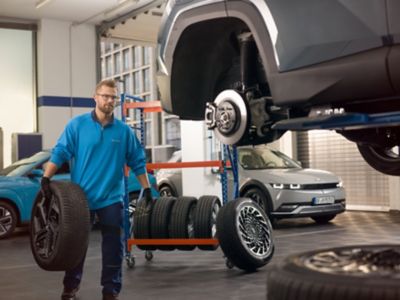 Mechanik Hyundai nesúci koleso k automobilu v dielni pri výmene pneumatík.
