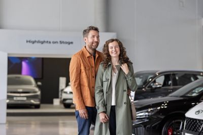 Ein Mann und eine Frau in Jacke und Mantel stehen lachend eng nebeneinander in einem Hyundai Autohaus.