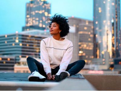 A woman sitting in front of a city skyline enjoying the reduced urban noise due to EV mobility.