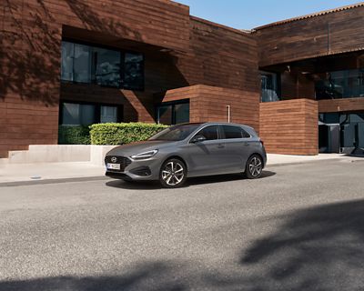 Vue de trois-quarts avant de Nouvelle Hyundai i30 en gris, garée à l'extérieur d'une maison moderne.
