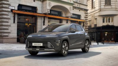 The all-new Hyundai KONA electric parked in front of a lake with a woman standing next to it.