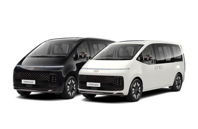 Ein schwarzer und ein weißer Hyundai STARIA, schräg von vorne gesehen.