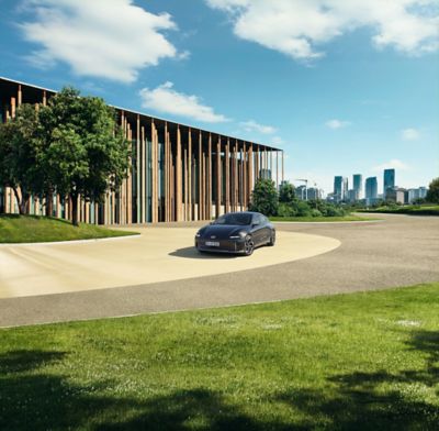 Der Hyundai IONIQ 6 vor einem holzverkleideten, modernen Gebäude am Stadtrand.