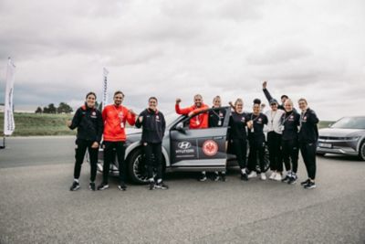 Sich freuende Eintracht Frankfurt Spielerinnen und Spieler stehen vor einem Hyundai Fahrzeug mit Hyundai und Eintracht Logo und geöffneter Seitentür