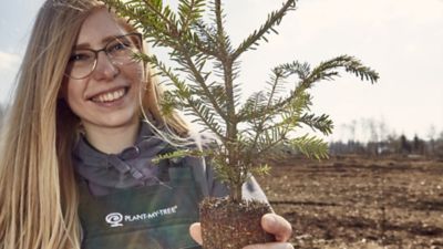 Eine PLANT-MY-TREE® Mitarbeiterin mit einem Baumsetzling.