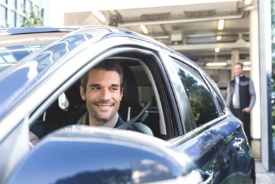 Ein Mann sitzt nach einem Servicetermin beim Hyundai Service-Partner zufrieden auf dem Fahrersitz  und lächelt.