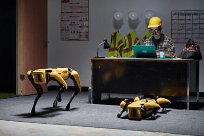 worker sitting at a desk with two four-legged Spot robots waiting for instructions