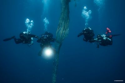 Traja potápači vyberajúcu odtrhnutú rybársku sieť z oceánu.
