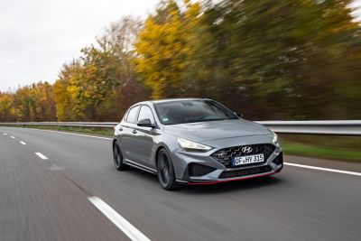 Ein grauer Hyundai i30 Fastback N auf einer baumbestandenen Landstraße.