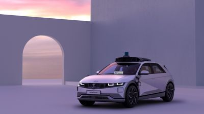 A woman and a Spot robot approaching an IONIQ 5 robotaxi outside a suburban house.