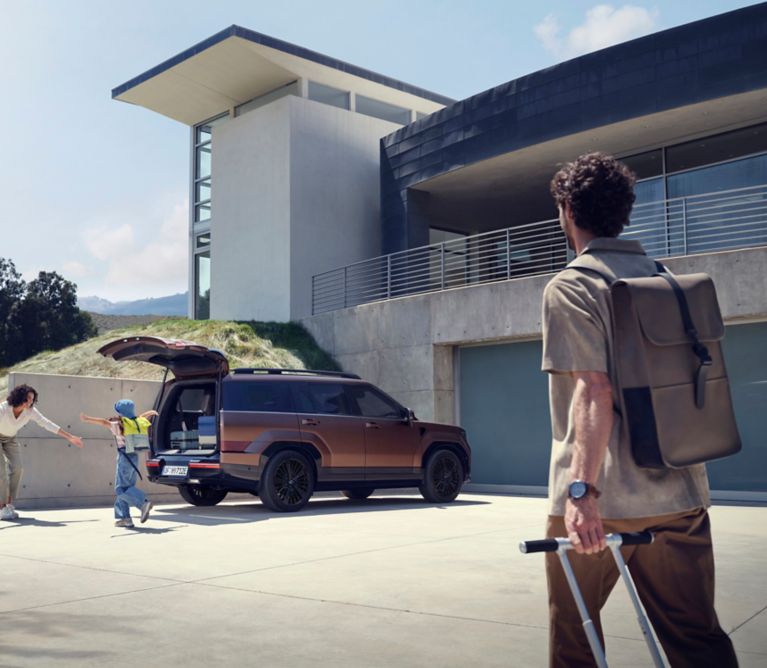 Matka s dietatom pri nakladani batoziny do zadneho kufra SANTA FE, otec kracajuci s kufrom smerom k nim