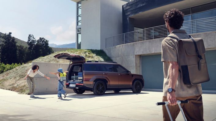 Matka s dietatom pri nakladani batoziny do zadneho kufra SANTA FE, otec kracajuci s kufrom smerom k nim