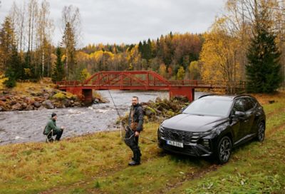 Två personer fiskar i en älv. En Hyundai TUCSON står parkerad intill älven.