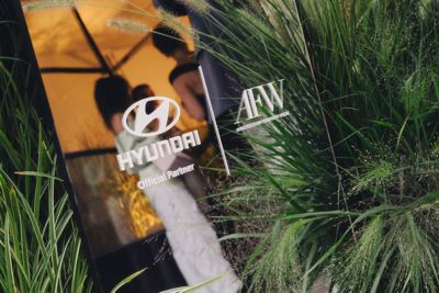 Logo’s Hyundai en Amsterdam Fashion Week op een raam met op de achtergrond twee personen.