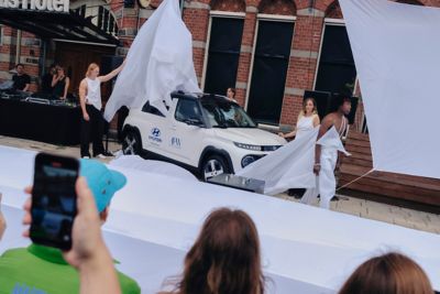 Modellen in kleding van modemerk MARTAN trekken het doek van een Hyundai INSTER naast een catwalk.