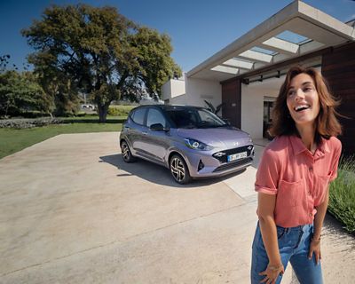 Une femme marche et sourit devant la nouvelle Hyundai i10.