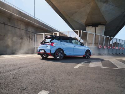 A young woman sitting on the hood of an Hyundai i20 N with a young man leaning on the open door.