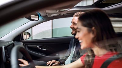 L'intérieur d'une Hyundai à travers la vitre du passager, un couple à l'intérieur regardant l'écran tactile.