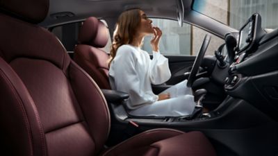 Une femme est assise à la place du conducteur de sa Hyundai i 30 Fastback en stationnement et regarde dans le rétroviseur à sa visière.