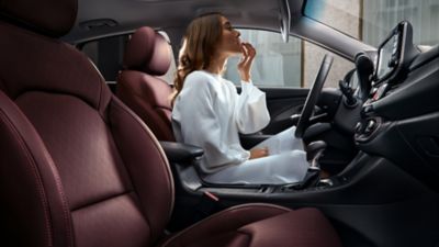 Woman sitting in the driver seat of her parked Hyundai i 30 Fastback, looking in the mirror on her visor.