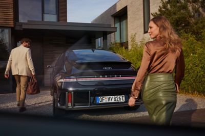 Un hombre vestido con traje claro frente al Hyundai IONIQ 6 y mujer con falda verde detrás de él. 