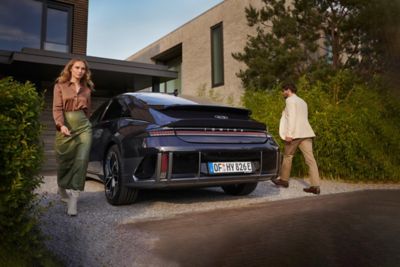 woman with brown t-shirt and a man standing next to the Hyundai IONIQ 6 