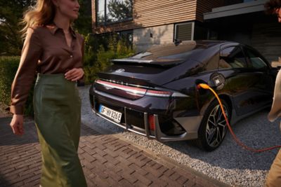 Woman with brown t-shirt and green skirt walking behind the black Hyundai IONIQ 6