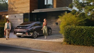 Man and woman standing in front of Hyundai IONIQ 6 connected to the charging cable and parked in the driveway.