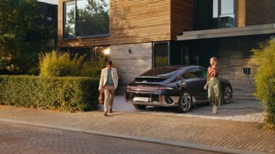 IONIQ 6 charges in front of a house driveway while a man and a woman wallk away.