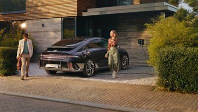 Mujer caminando junto al nuevo KONA Eléctrico, aparcado en la calle.