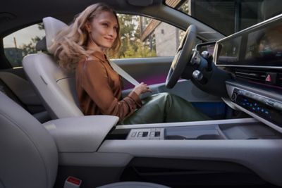 Une femme avec un t-shirt marron et une jupe verte sur le siège conducteur de la Hyundai IONIQ 6. 